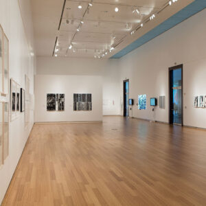  Image of an art gallery with white walls, wood floors, and a high ceiling.