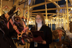Mic doing a condition report on the carousel. She is surrounded by carousel animals.